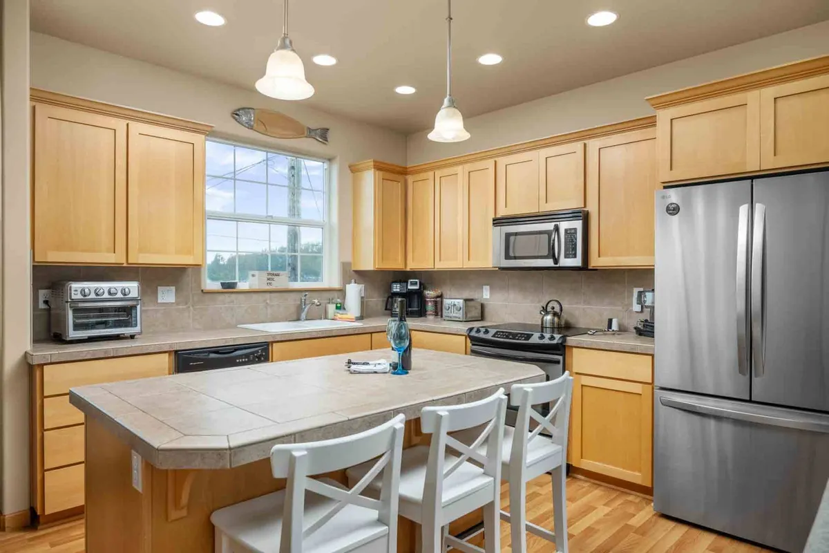 A welcoming kitchen with a spacious island, stainless steel appliances, and wooden cabinetry. A large window offers a scenic view, seamlessly connecting the cooking area with the outdoors and providing a bright, cheerful atmosphere.