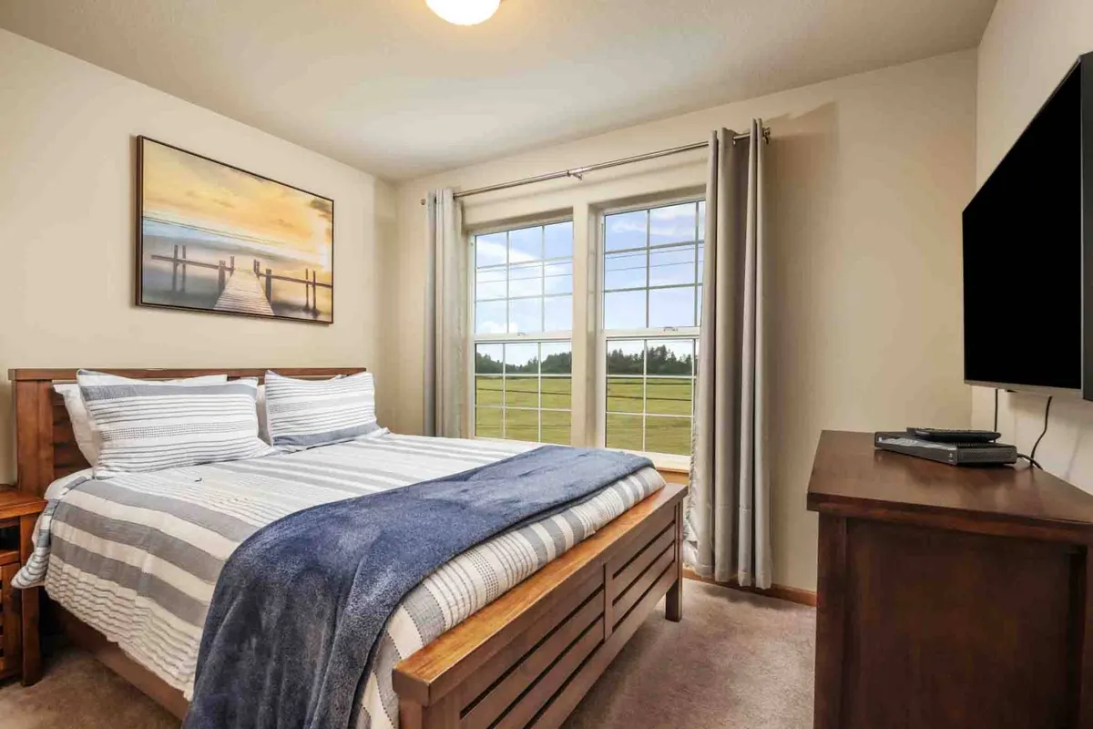 A tranquil queen bedroom with a comfortable bed, a window allowing in gentle natural light, and a painting on the wall. The room offers peaceful ambiance for relaxation, reading, or watching TV, with a sense of privacy and rejuvenation.