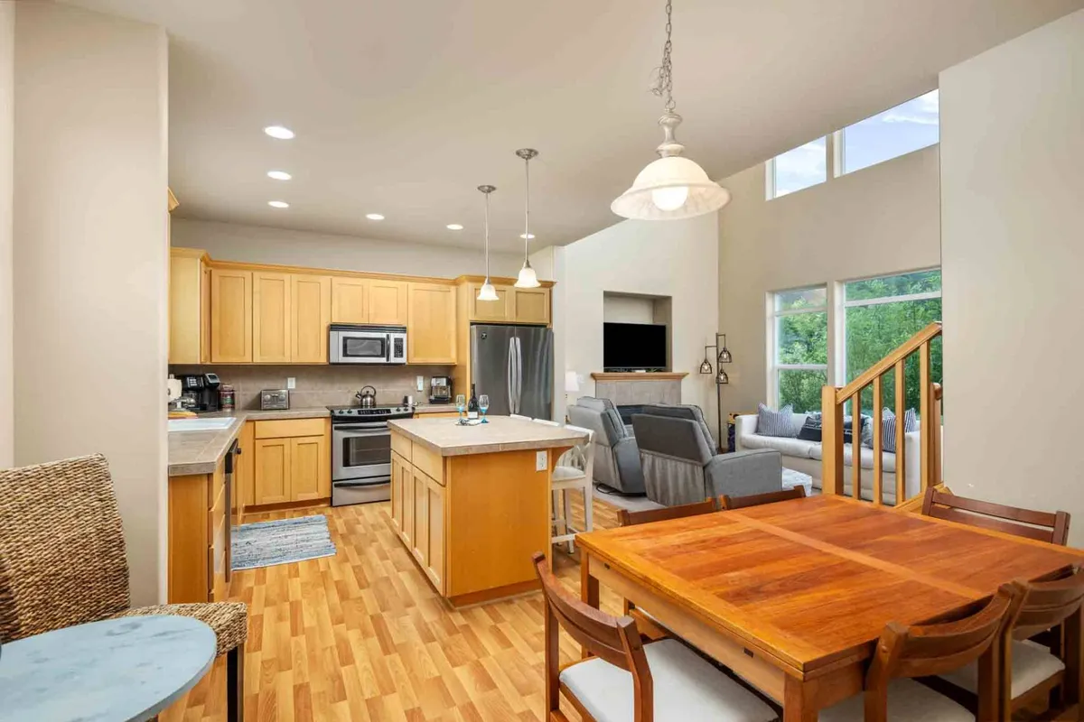 This image showcases the kitchen island and dining table set against a backdrop of large windows, allowing natural light to flood the open space. The inviting layout encourages both cooking and socializing, and the view through the windows hints at a scenic outdoor setting.