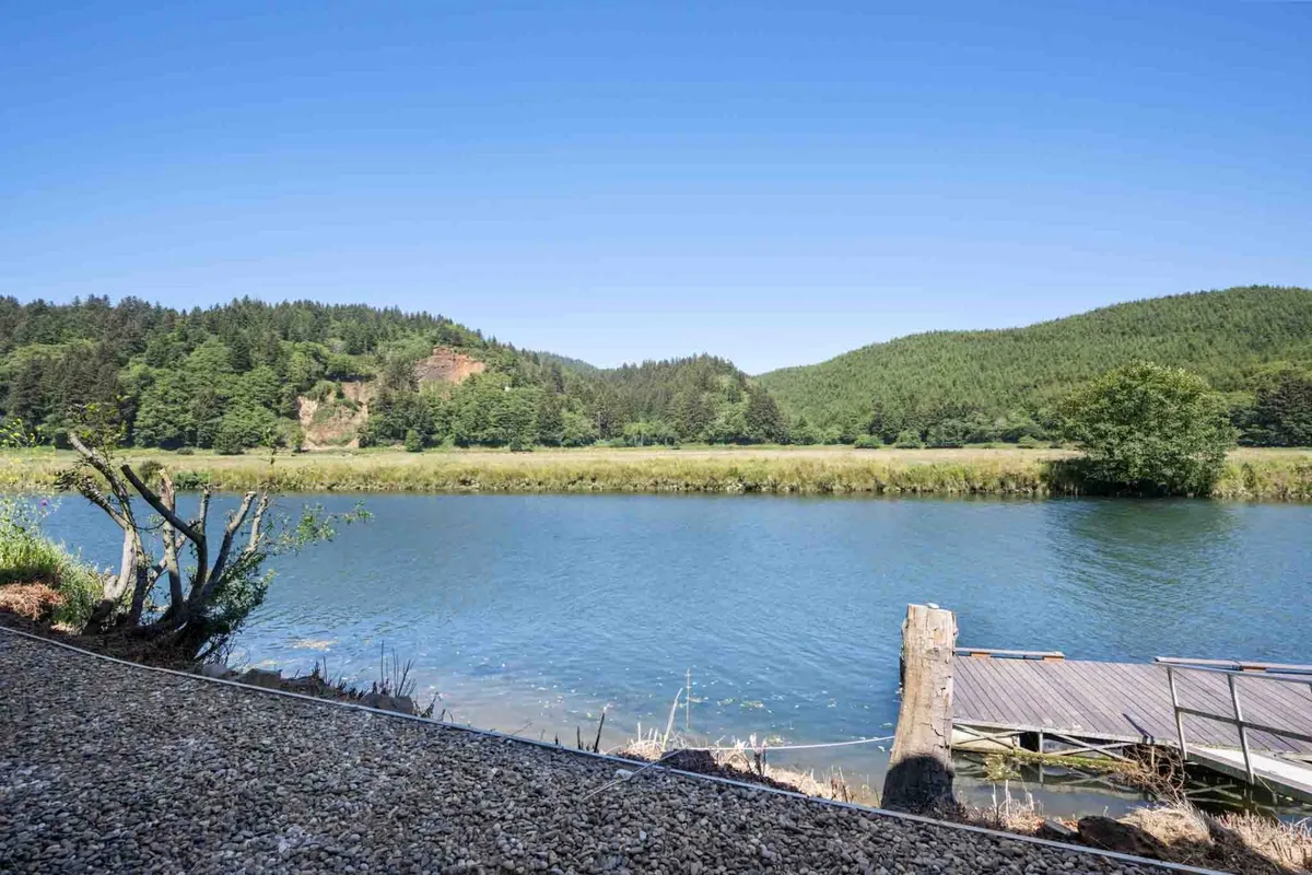 A tranquil view of the calm river with a wooden pier stretching over the water, surrounded by lush greenery and rolling hills. The scene invites activities such as fishing, kayaking, and bird watching, set in a peaceful, natural environment ideal for riverfront adventures.