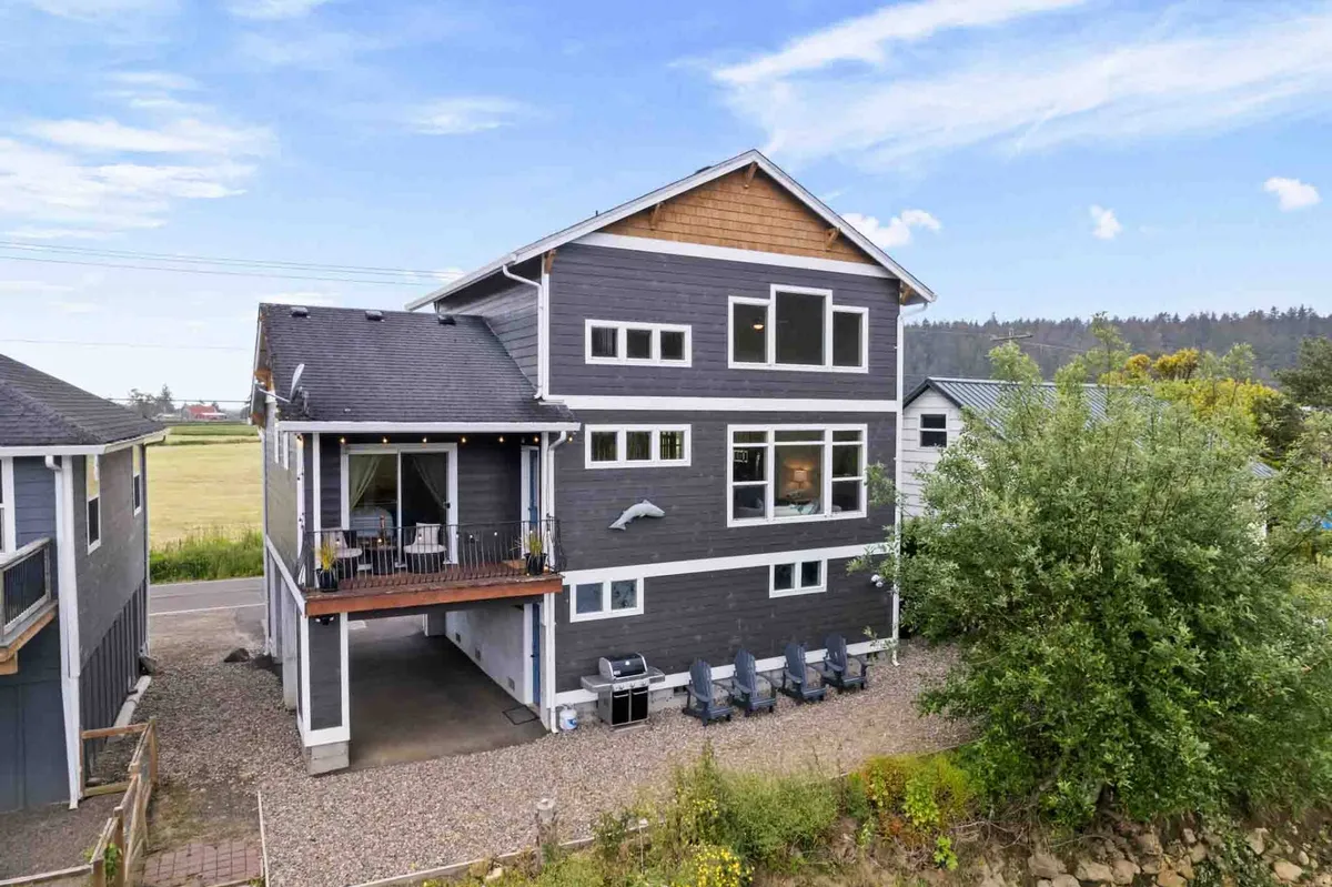 An inviting exterior shot of the property showing large windows, a deck with comfortable seating, and a landscaped area. The deck overlooks scenic surroundings, perfect for relaxing after outdoor adventures with pets.